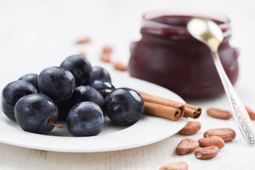 Fresh plums, cinnamon sticks, raw cocoa beans and homemade plum jam on white background