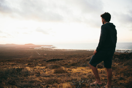 Man standing at valley and looking afar at seascape at sunset