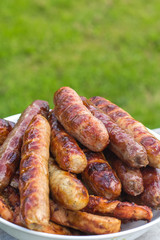 Freshly roasted ruddy sausages. In a plate. Against the background of green grass
