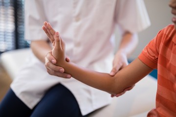 Midsection of female therapist examining wrist while boy sitting