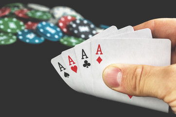 Four aces in hand with poker chips on black blurred on background. Casino win concept 