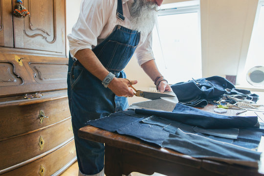 Closeup of Cool Senior Man Cutting Denim Fabric on Living Room Table