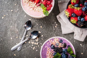 Ideas for healthy summer breakfast. Smoothies in bowls wth red (strawberry raspberry currant), blue (blueberry blackberries) berry With oatmeal, fresh berries. Dark stone table. Top view copy space