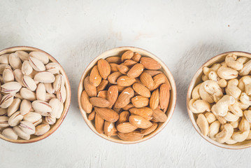 Selection nuts on a white stone table, in a bowl and scattered: almond, cashew and pistachio. Copy space top view