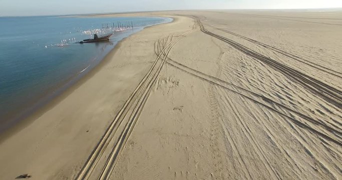 Aerial view drone video of Pelican Point Lodge and Paratus lighthouse on sand beach peninsula, shipwreck and lagoon with ocean background with ships at Namibia's Atlantic west coast