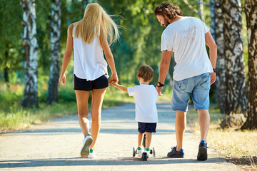 Happy family in the park. Parents with a child on a scooter are walking in nature.