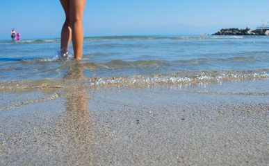 Girls naked bare legs standing in crystal clear water on the beach on a sunny day