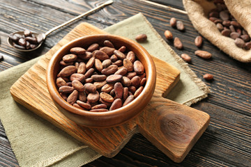 Bowl with aromatic cocoa beans on wooden background