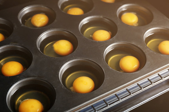 Muffin tin with raw eggs in oven, closeup