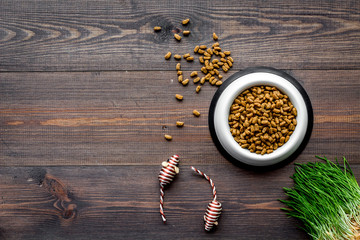 bowl full and overflowing with dry pet - cat food bits and mouse toys on wooden background top view mock-up