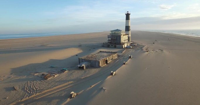 Aerial view footage of desert sand peninsula, old lighthouse and power station building on ocean seals beach, Walvis Bay lagoon view with sea background and ships at Namibia's Atlantic west coast