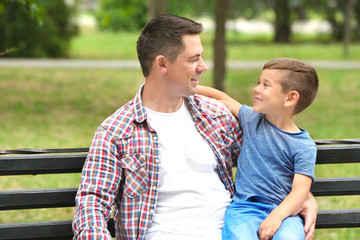 Obraz premium Father and son sitting on wooden bench outdoors