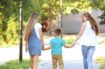 Happy lesbian mothers and foster son walking in park. Adoption concept