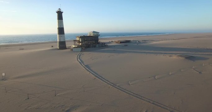 Aerial view footage of desert sand peninsula, old lighthouse and power station building on ocean seals beach, Walvis Bay lagoon view with sea background and ships at Namibia's Atlantic west coast