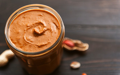 peanut butter on a table in a glass jar with peanuts around