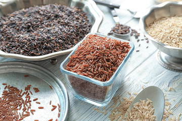 Different types of rice in bowls, plate and spoons on wooden table