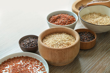 Different types of rice in bowls and plate on wooden table