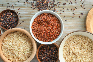 Different types of rice in bowls on wooden table