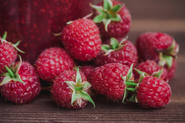 Summer raspberry fruits on wooden desk with glass jam jar in the background.