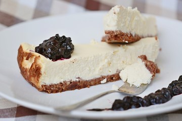 Homemade baked cheesecake with blueberry topping on white plate with fork