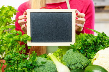Woman having green vegetables holding board