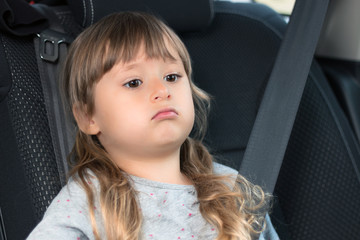 A beautiful little girl is sitting in the car wearing a seat belt. Safety and protection of children. Portrait.