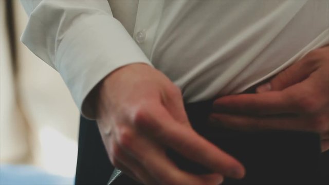 Businessman puts on a belt on trousers