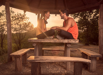 two people, young couple, smiling, sitting on wood table, outdoors, warm sunny day Sun, relaxing, sport clothes