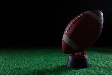 Close-up of American football standing on holder on artificial