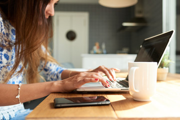 Brunette working on laptop with cup of coffee or tea on table