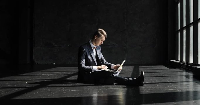 Successful young Man Working In Home Office in loft style. Stylish hipster man in a suit working against a blavk wall background lit by sunlight