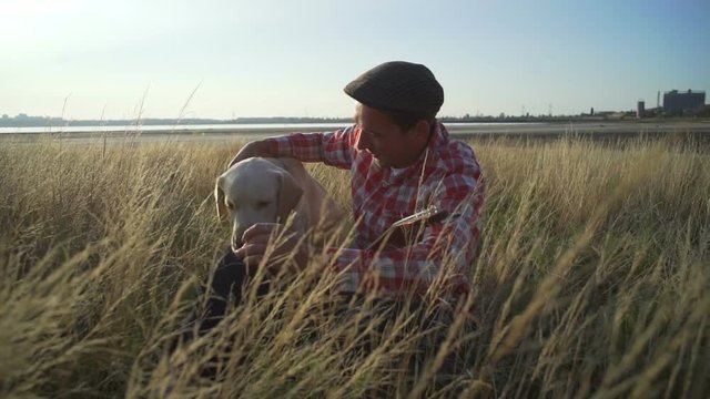 Man with ukulele playing with labrador dog at wheat field rapid slow motion  