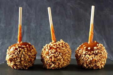 Three festive caramel apples with nuts against a dark slate background