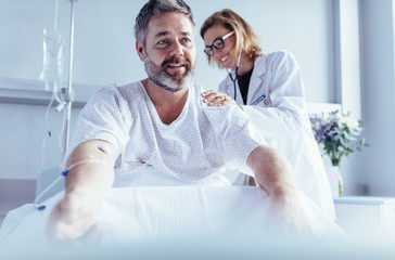 Mature man sitting in hospital bed and physician doing checkup. - Powered by Adobe