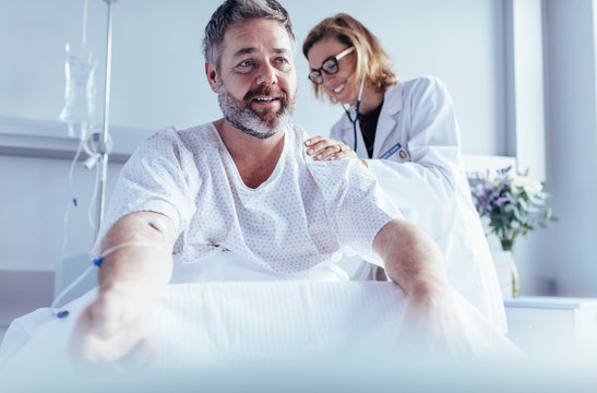 Mature man sitting in hospital bed and physician doing checkup.