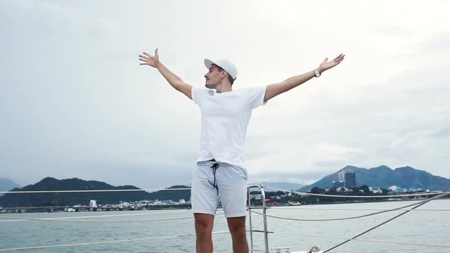 Young man looking at the ocean and hold hands up in the air on yacht