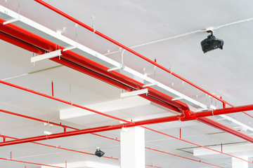 Fire sprinkler system with red pipes is placed to hanging from the ceiling inside of an unfinished new building. - obrazy, fototapety, plakaty
