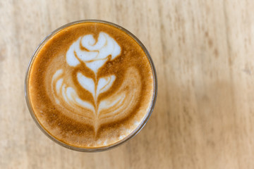 A cup of coffee with latte art rose flower pattern in a white coffee cup on wooden table in coffee shop