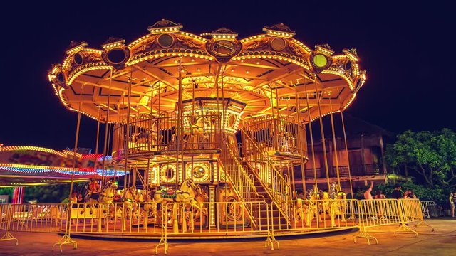 4K Resolution time lapse, Cinemagraph long exposure. Flying house carousel is playing the lighting to go spin a round and stop at night, celebrate and funny carnival background with vintage filter.