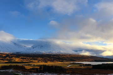 Incredible landscape view of the Scottish Highlands with snow capped mountains, low hanging clouds, and glowing fields during sunrise in the early winter.