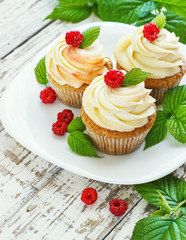 Delicate vanilla cupcakes with cream and raspberries on a white wooden background