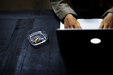 Hands using computer laptop by the cigarette ash tray