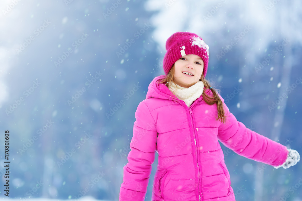 Wall mural Adorable little girl having fun in beautiful winter park. Cute child playing in a snow.