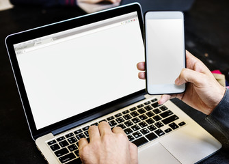 Hands holding mobile phone with computer laptop background