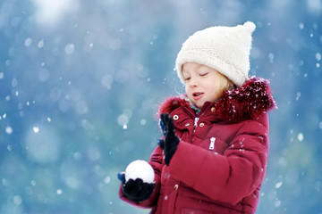 Adorable little girl having fun in beautiful winter park. Cute child playing in a snow.