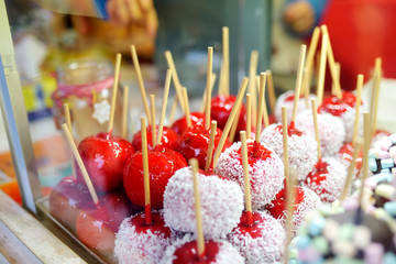 Apples dip in red sugar icing and coconut chips sold on Christmas market. Candies, sweets and...