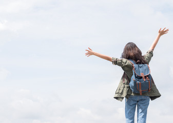 Back side of young girl with blue rucksack on her back wave hands up with blue sky