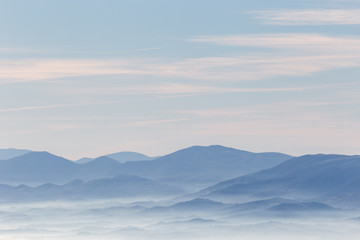 Widok z góry na dolinę wypełnioną morzem mgły, z różnymi warstwami wschodzących wzgórz i gór o różnych odcieniach niebieskiego - 170807210