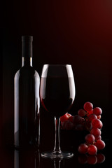Bottle of red wine, a glass of red wine and grapes on a dark background.