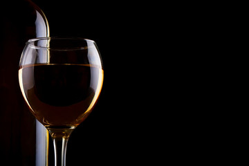 A bottle of white wine and a glass of white wine on a dark background.